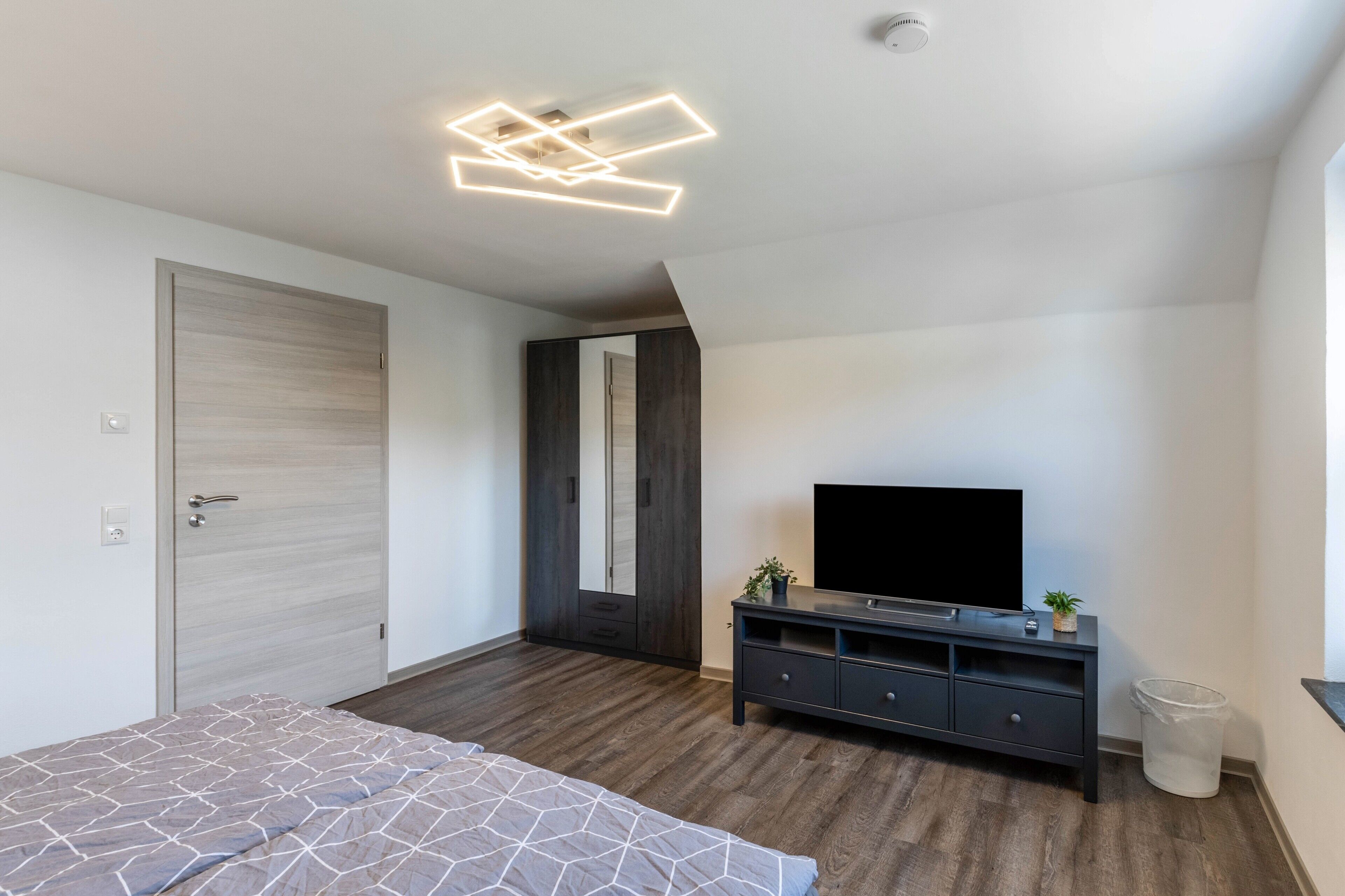Ein modernes Schlafzimmer mit Bett, Fernseher, Kleiderschrank und Spiegel.