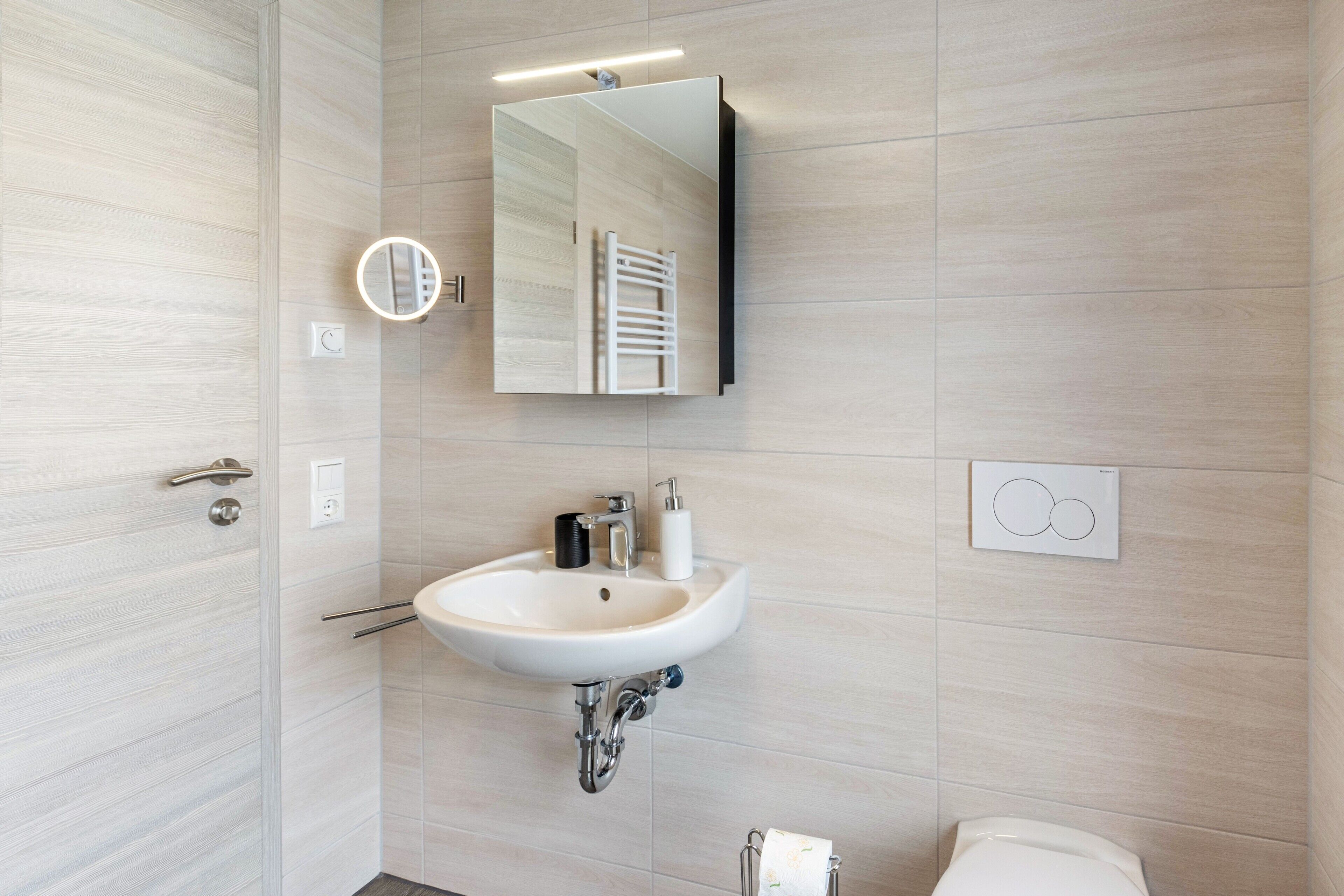 Ein modernes Badezimmer mit Waschbecken, Spiegel, Handtuchhalter und Toilette.