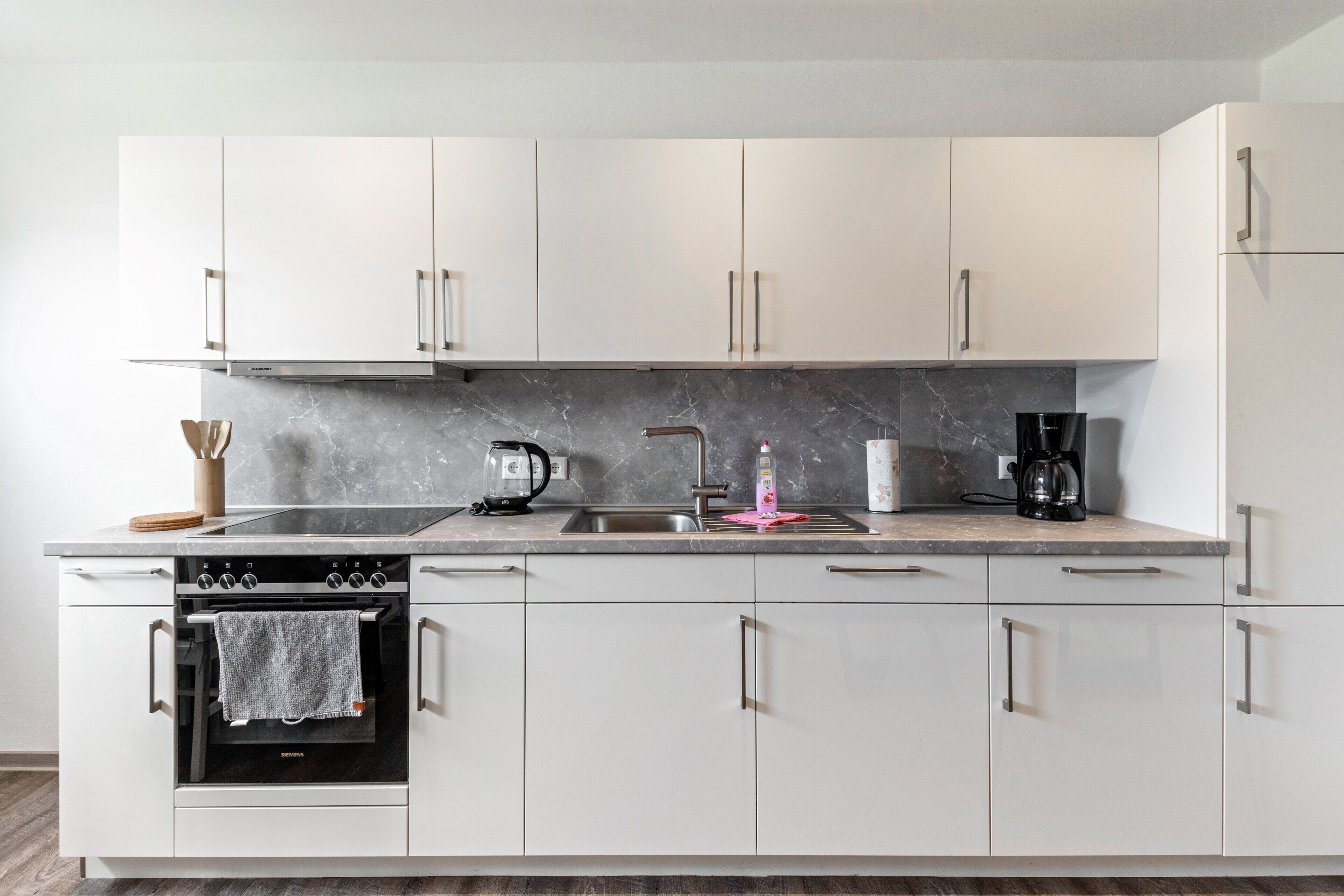 Eine moderne Küche mit weißen Schränken, einem Backofen, einer Kaffeemaschine und einem Spülbecken.