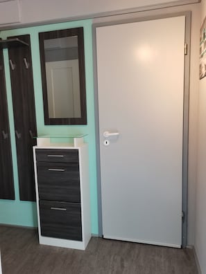 Una habitación con una puerta blanca, un espejo y un mueble blanco con cajones.