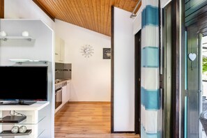 A modern kitchen with white cabinets, a wooden ceiling, and a large flat-screen TV on a glass stand.