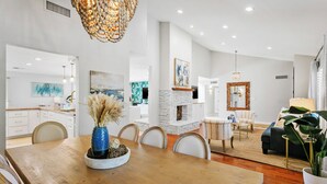 A modern dining area with a wooden table, chairs, and a vase with dried plants. There is a stone fireplace, a sofa, and a coffee table in the background. - SWSS 4BR Kierland Luxury Escape | Heated Pool, Game Room, Putting Green (Scottsdale)