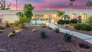 A modern house with a stone facade, a driveway, and a garden with various plants and a palm tree. - SWSS 4BR Kierland Luxury Escape | Heated Pool, Game Room, Putting Green (Scottsdale)