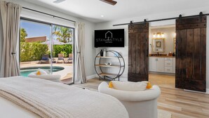 A modern bedroom with a large bed, a TV, and a sliding door leading to a bathroom. - SWSS 4BR Kierland Luxury Escape | Heated Pool, Game Room, Putting Green (Scottsdale)