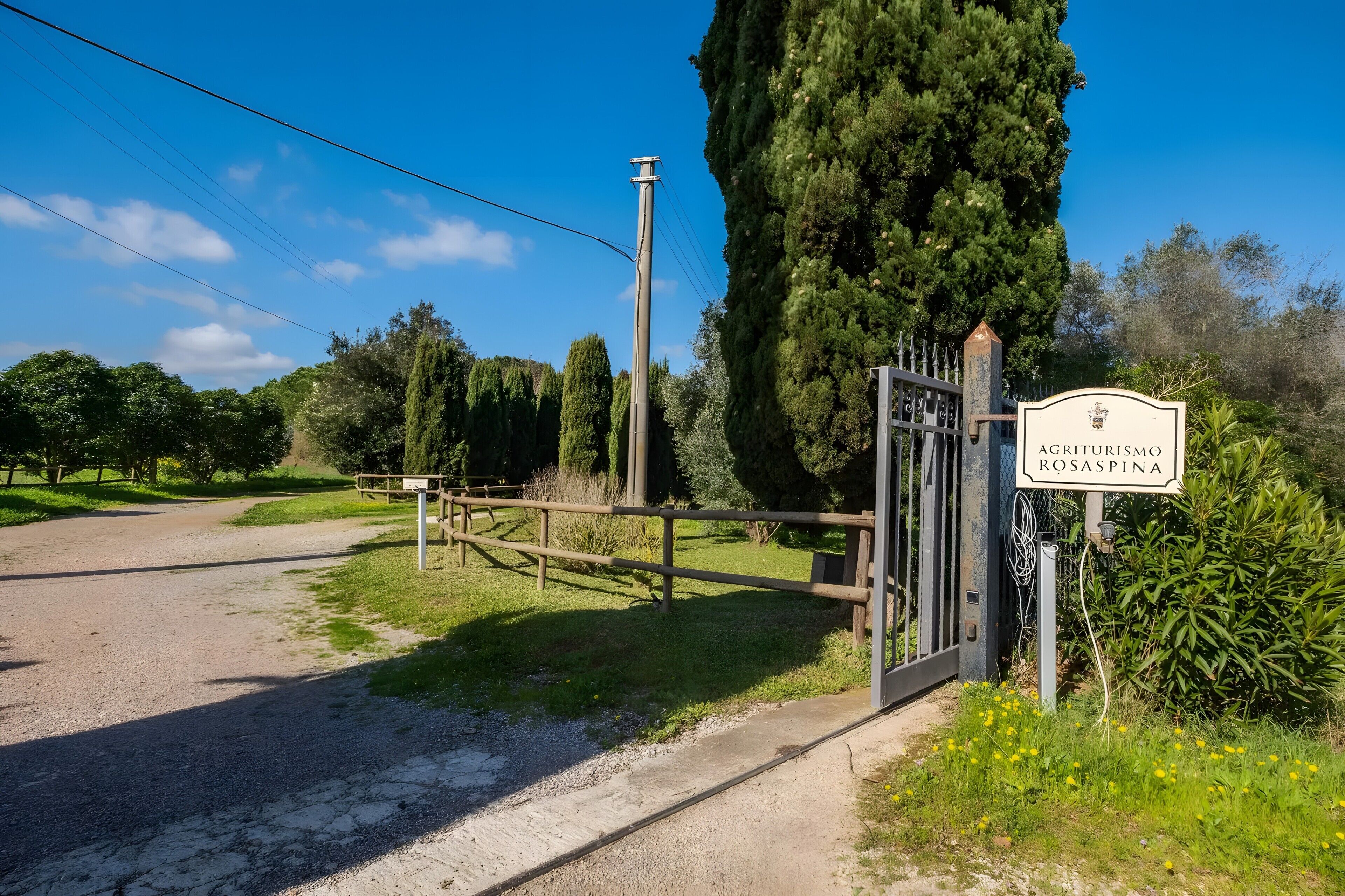 A rural road leading to a gated property named 'Agriturismo Rosaspina.'