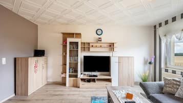 Una sala de estar con televisor, muebles de madera, una estantería y un sofá.