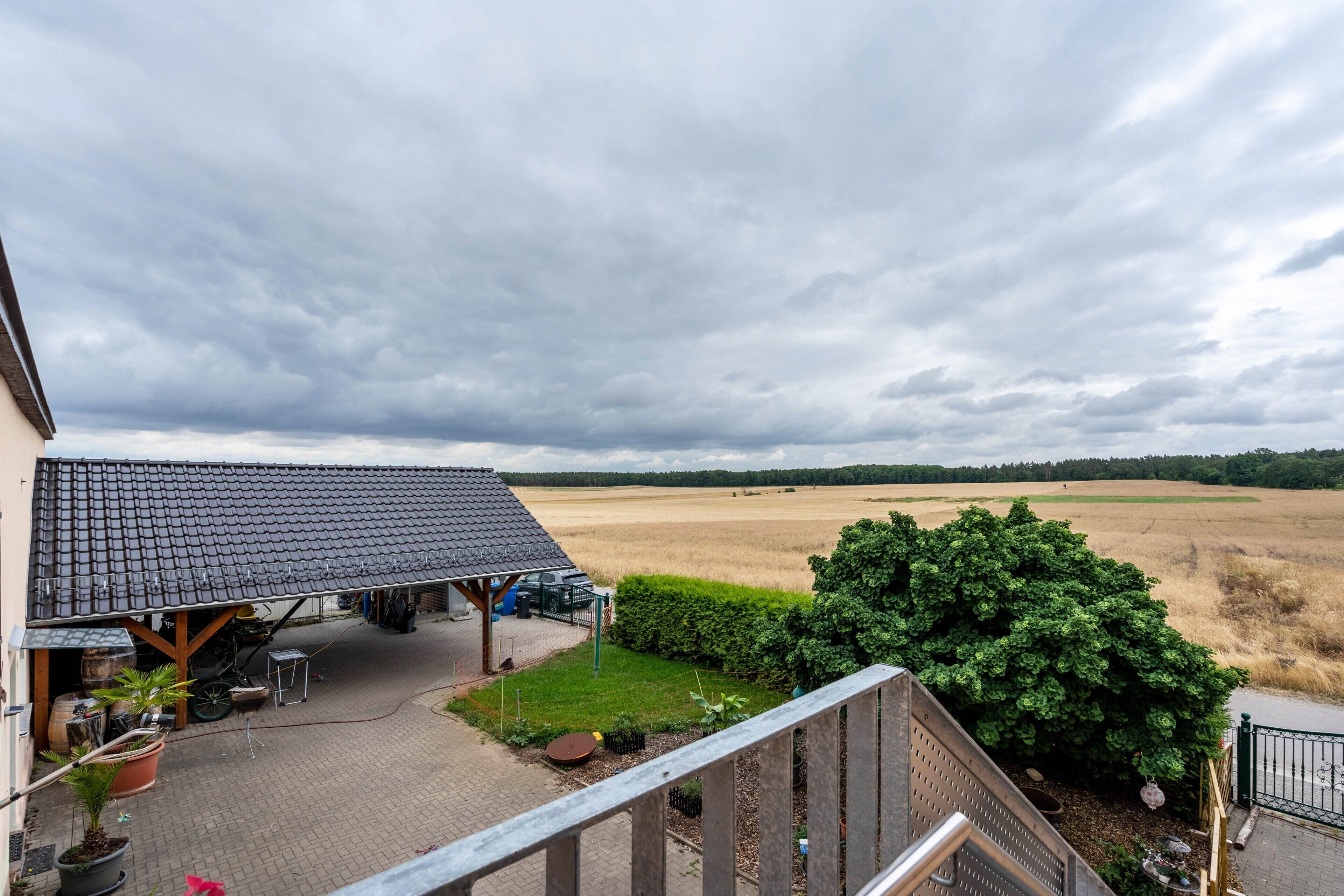 Ein Gebäude mit Ziegeldach, einer überdachten Terrasse und Blick auf ein Feld.