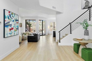 A spacious living area with a modern staircase, a large abstract painting, and a view of the outdoors.