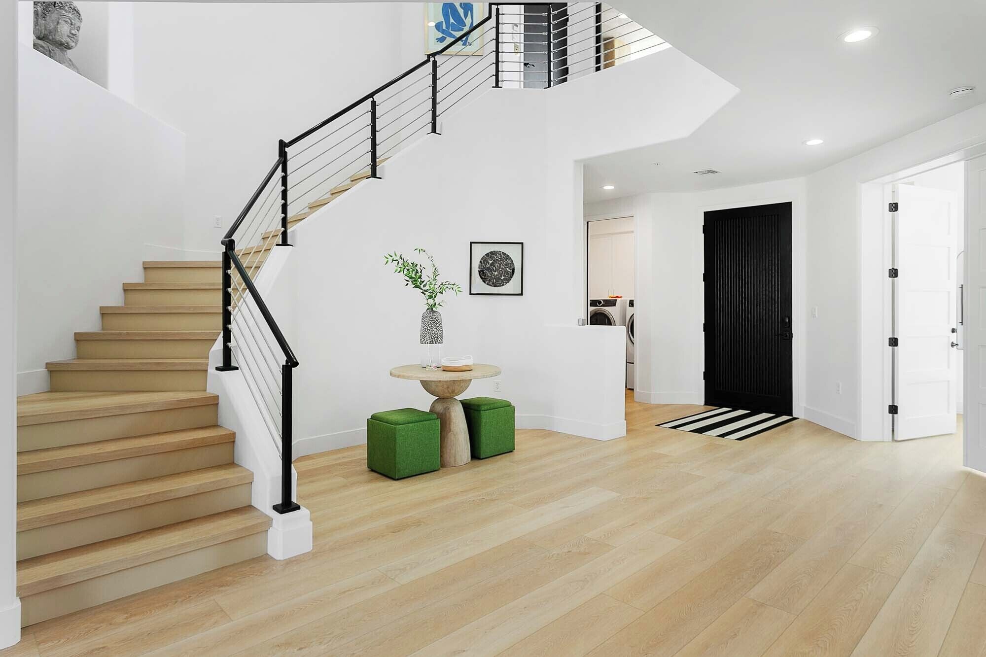 Un intérieur moderne avec un escalier en bois, une table ronde ornée d’un vase et une porte noire.