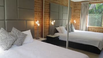 A hotel room with two beds, a brick wall, a large mirror, and a window with curtains.