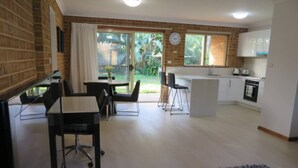 A modern kitchen with a dining area, a small office space, and a view of the garden. - Spacious 3 bedroom beach apartment. (Mona Vale)