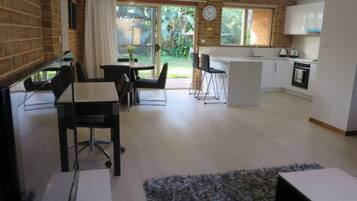 A modern kitchen with a dining area, a small office space, and a view of the garden.