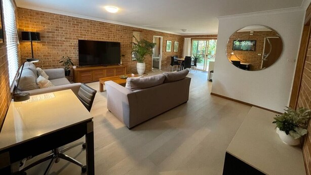 A modern living room with a sofa, a dining table, and a TV. - Spacious 3 bedroom beach apartment. (Mona Vale)
