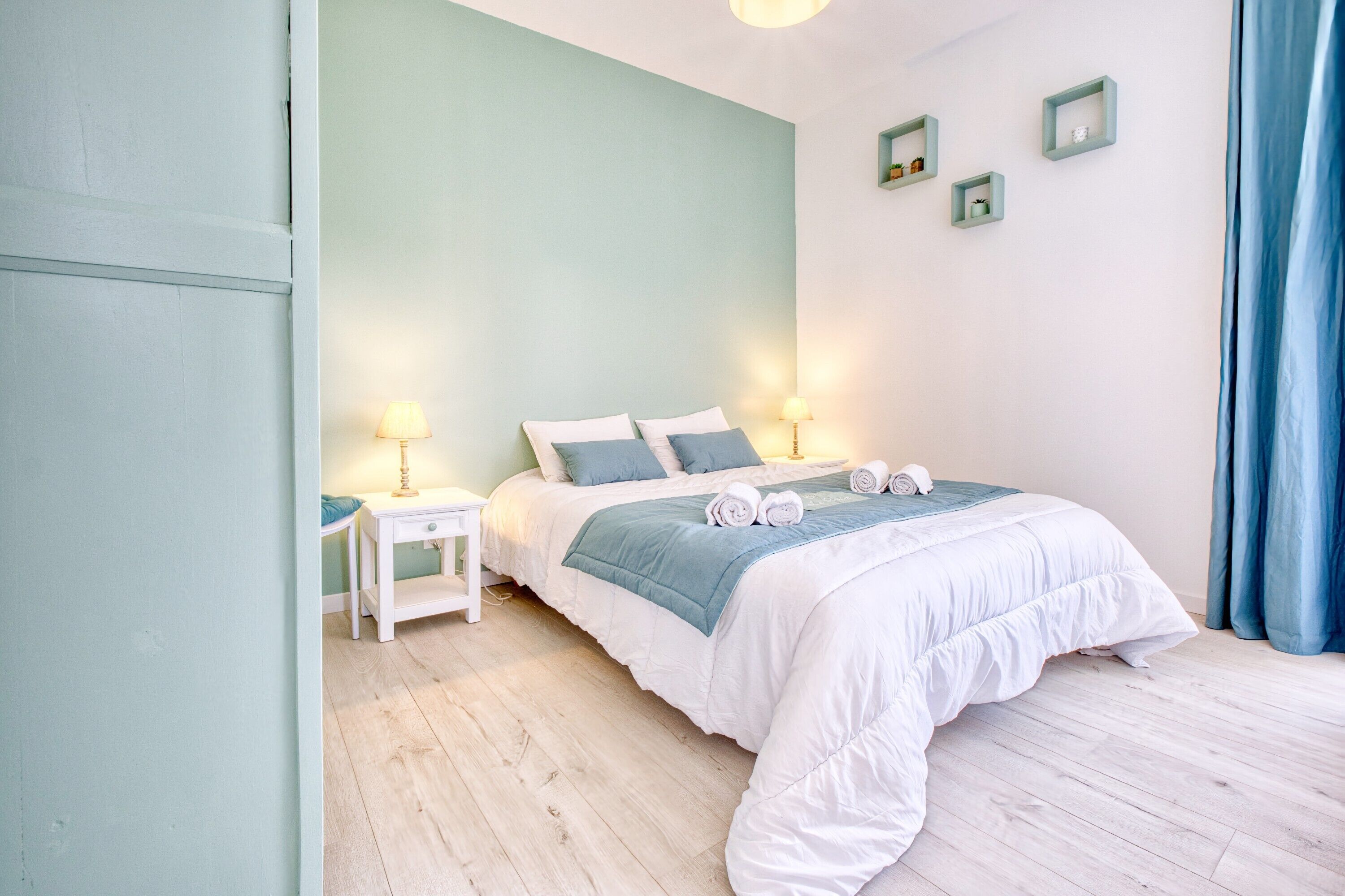 Um quarto com cama, mesas de cabeceira, luminárias e cortina azul.