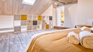 Een kamer met een schuine kap, een bed met een beige sprei, een dakraam en opbergkasten met lades.