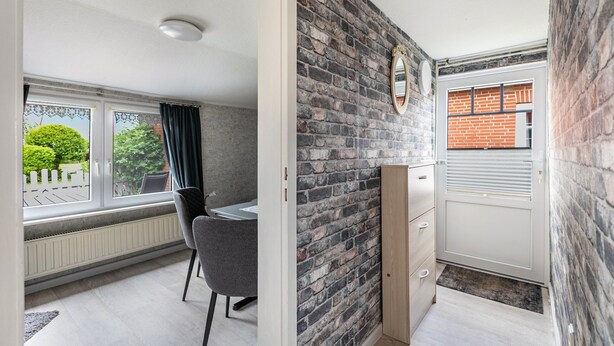 Une pièce avec un mur en briques, une fenêtre avec des rideaux, une porte avec une vitre et un radiateur.
