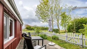 Une terrasse avec une table et des chaises, un barbecue, une clôture blanche en bois et un arbre.
