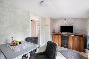 Ein modernes Wohnzimmer mit Esstisch, zwei Stühlen, einem Flachbildfernseher und einer Holzkommode.