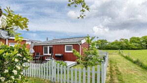 Une maison rouge avec une clôture blanche en piquets, un barbecue et une table avec des chaises sur la terrasse.