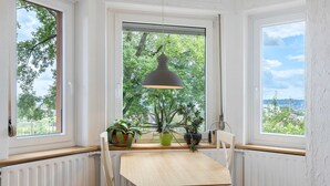 A corner room with a table and chairs, a pendant light, a window with a view of trees, and a radiator. - Apartment 'Rotes Haus' with Mountain View, Private Terrace and Wi-Fi (Konstanz)