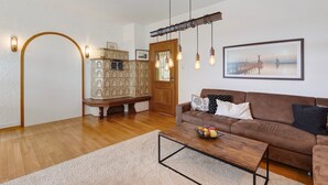 A living room with a brown sofa, a coffee table with fruit, a wooden cabinet, and a door with a view of a pier. - Apartment 'Rotes Haus' with Mountain View, Private Terrace and Wi-Fi (Konstanz)