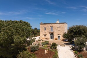 Un edificio de piedra con una puerta central, rodeado de árboles y un jardín.