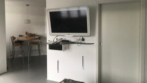 A modern living room with a mounted TV, a dining area with a table and chairs, and a door. - Apartment 'Bechtel' with Balcony and Wi-Fi (Langenargen)