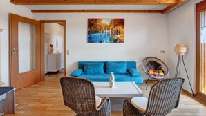 Une pièce avec un canapé bleu, des fauteuils en osier, une table basse blanche et un tableau représentant une cascade.