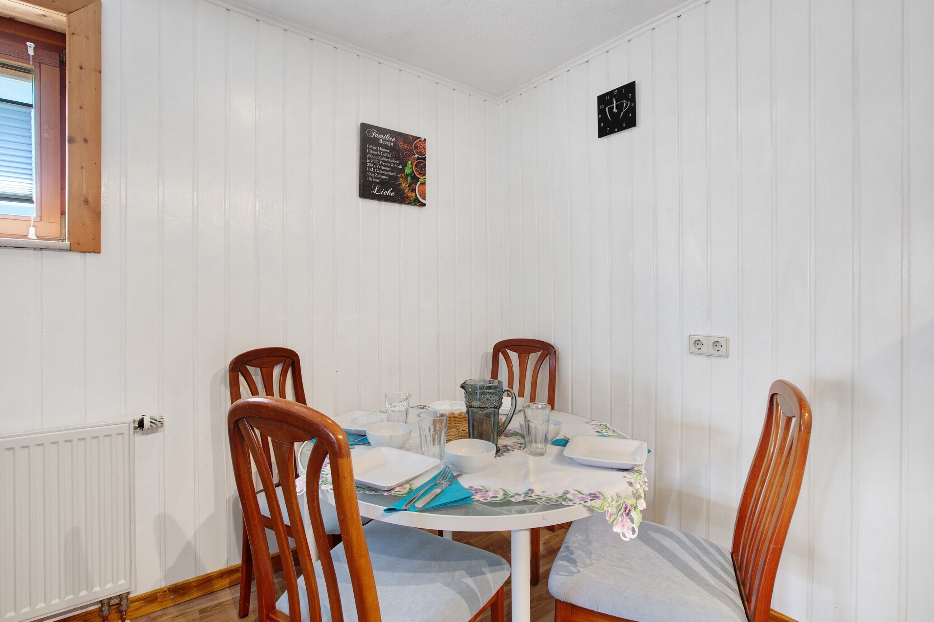 Un comedor con una mesa redonda, sillas, un tablero de menú y un reloj en la pared.