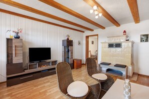 A living room with a flat-screen TV, wicker chairs, a wooden entertainment unit, and a fireplace. - Apartment 'Perla' with Mountain View, Private Terrace and Wi-Fi (Ühlingen-Birkendorf)