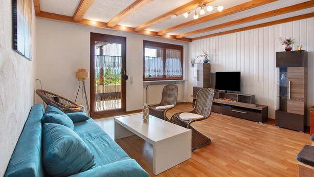 Un salon comprenant un canapé, des fauteuils, une table basse, un téléviseur et des poutres en bois au plafond.
