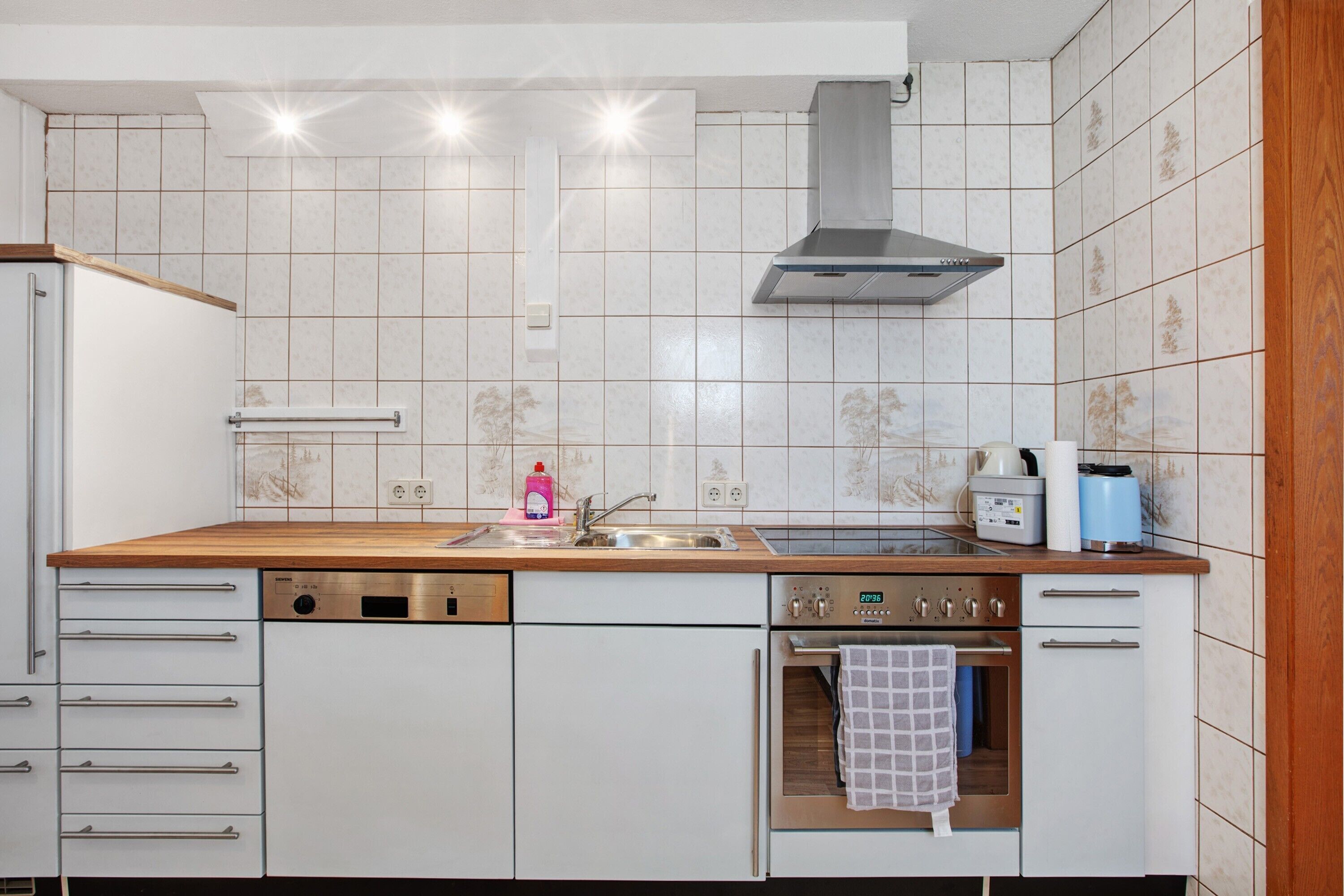 A kitchen with white cabinets, a wooden countertop, a stainless steel range hood, a dishwasher, an oven, and a sink.