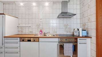 A kitchen with white cabinets, a wooden countertop, a stainless steel range hood, a dishwasher, an oven, and a sink.