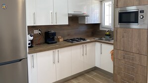 A modern kitchen with white cabinets, a built-in microwave, a coffee machine, and a gas stove. - Apartment 'Muscletes' with Mountain View, Wi-Fi and Air Conditioning (L'Escala)