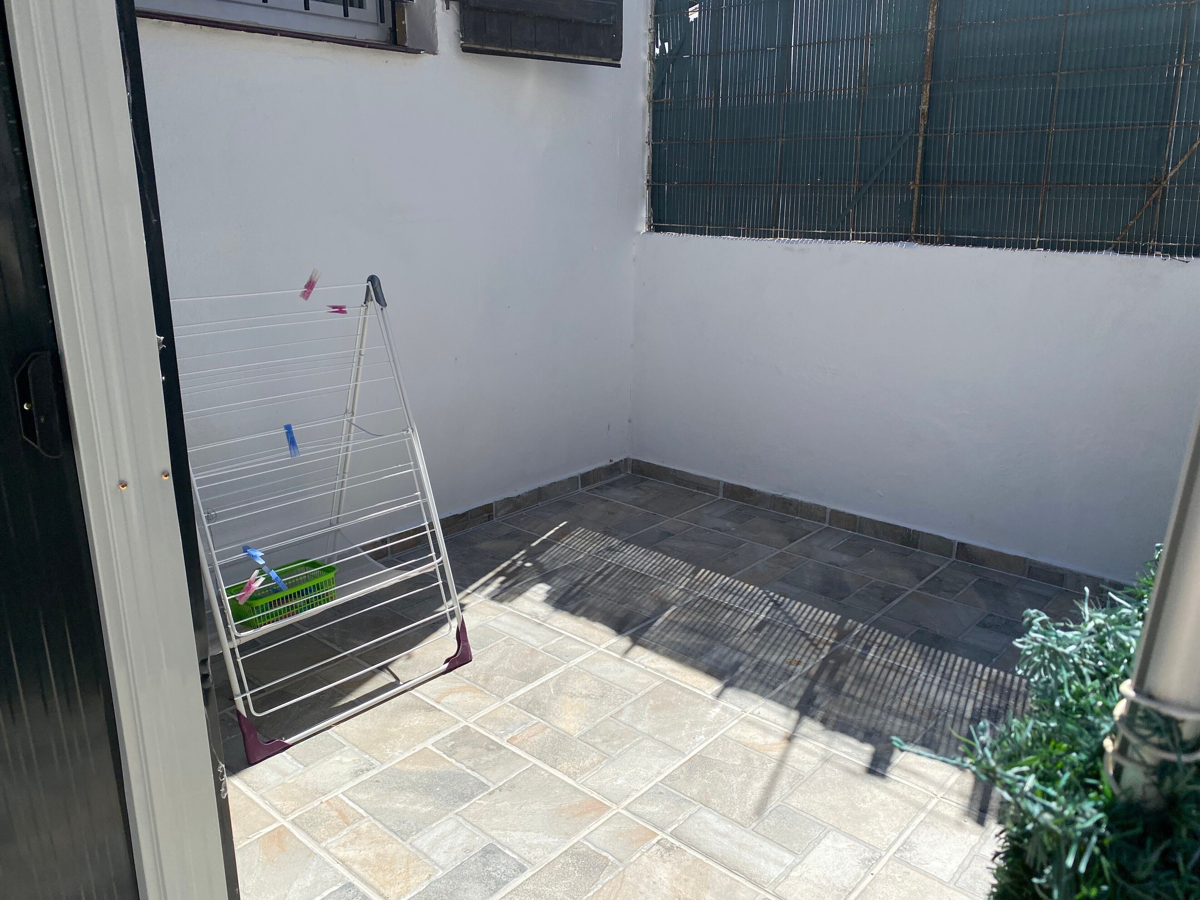 A small enclosed patio area with a metal rack, a green basket, and a window with metal bars.