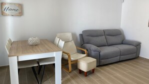 A room with a wooden dining table, a grey sofa, a white chair, and a small ottoman. - Apartment 'Muscletes' with Mountain View, Wi-Fi and Air Conditioning (L'Escala)