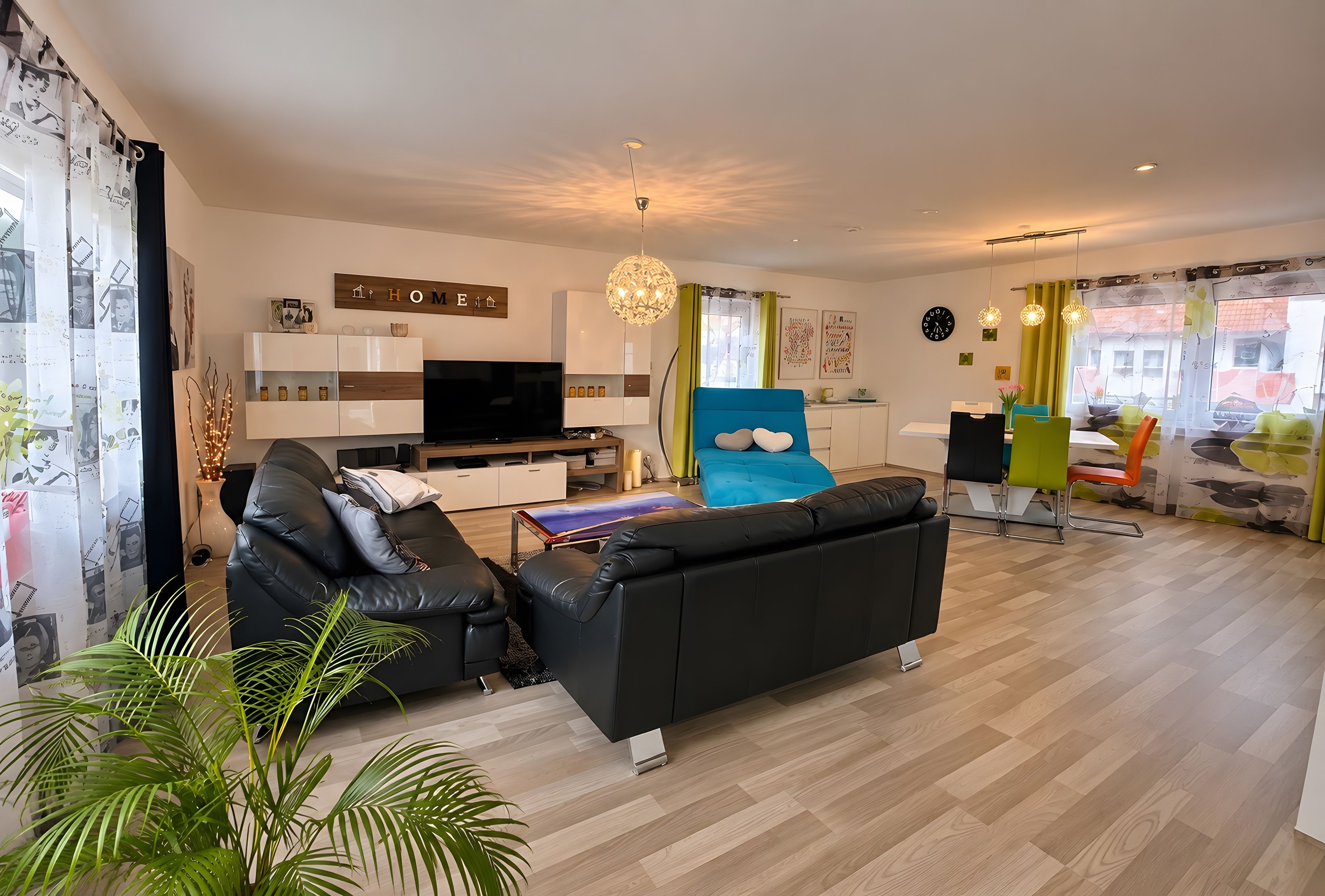 Un salon moderne avec un canapé noir, un téléviseur à écran plat et un coin repas agrémenté de chaises colorées.