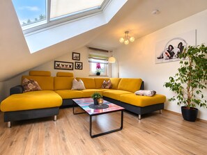 A modern living room with a yellow sectional sofa, a coffee table, and a large window with a view. - 5-Sterne-Ferienwohnung 'Dieterich 2' mit 2 Schlafzimmern und 27 m² großem Balkon (Beuren)