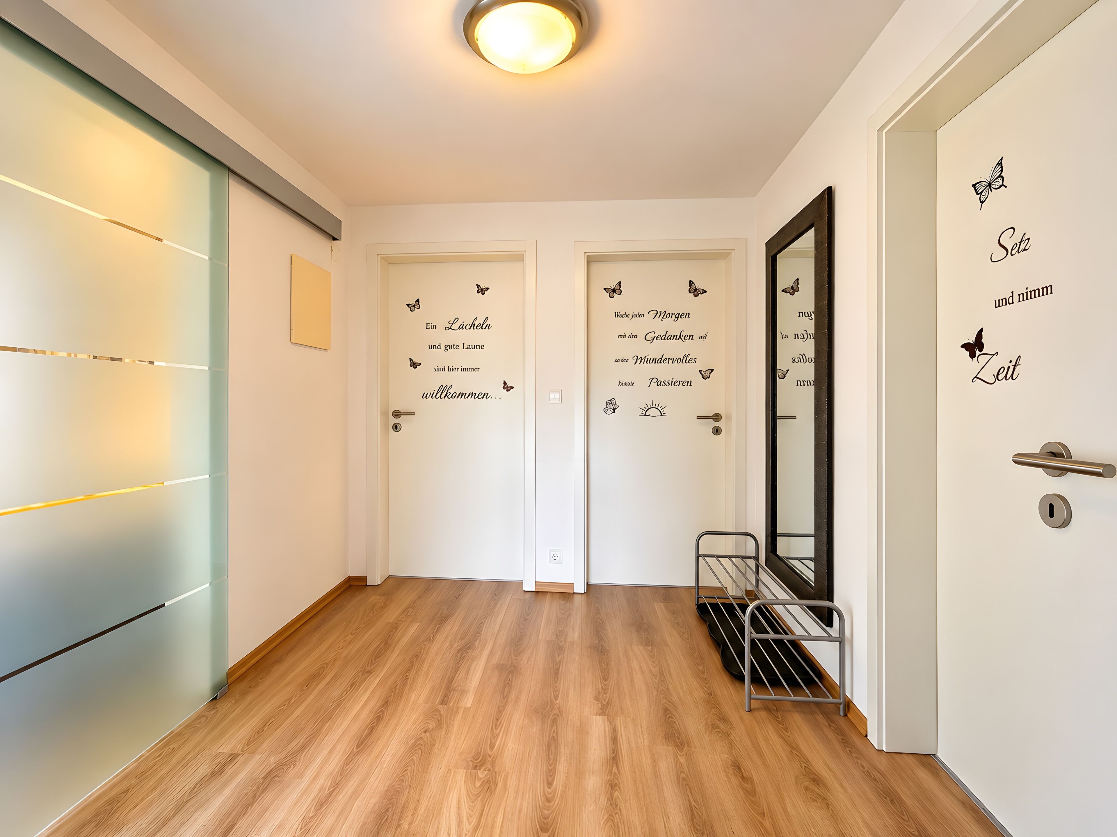 Un couloir doté d’un plancher en bois, de deux portes décorées d’autocollants représentant des papillons et d’une étagère en métal.