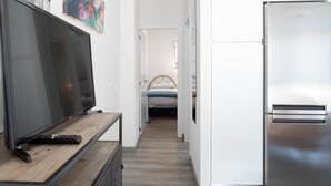 Ein enger Flur mit einem Fernseher auf einem Holzgestell, einem Kühlschrank und einem Bett mit blauer und weißer Bettdecke.