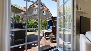 A room with a sliding glass door leading to a patio area, wicker furniture, a potted plant, and a television. - Holiday Home 'Huus Alex' with Private Terrace, Private Garden and Wi-Fi (St. Peter-Ording Dorf)