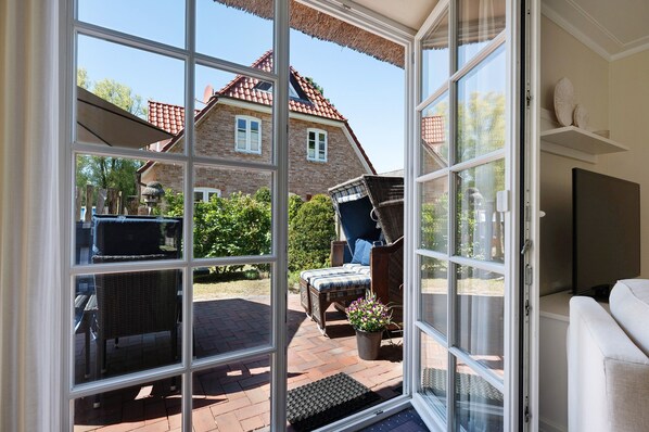 A room with a sliding glass door leading to a patio area, wicker furniture, a potted plant, and a television.
