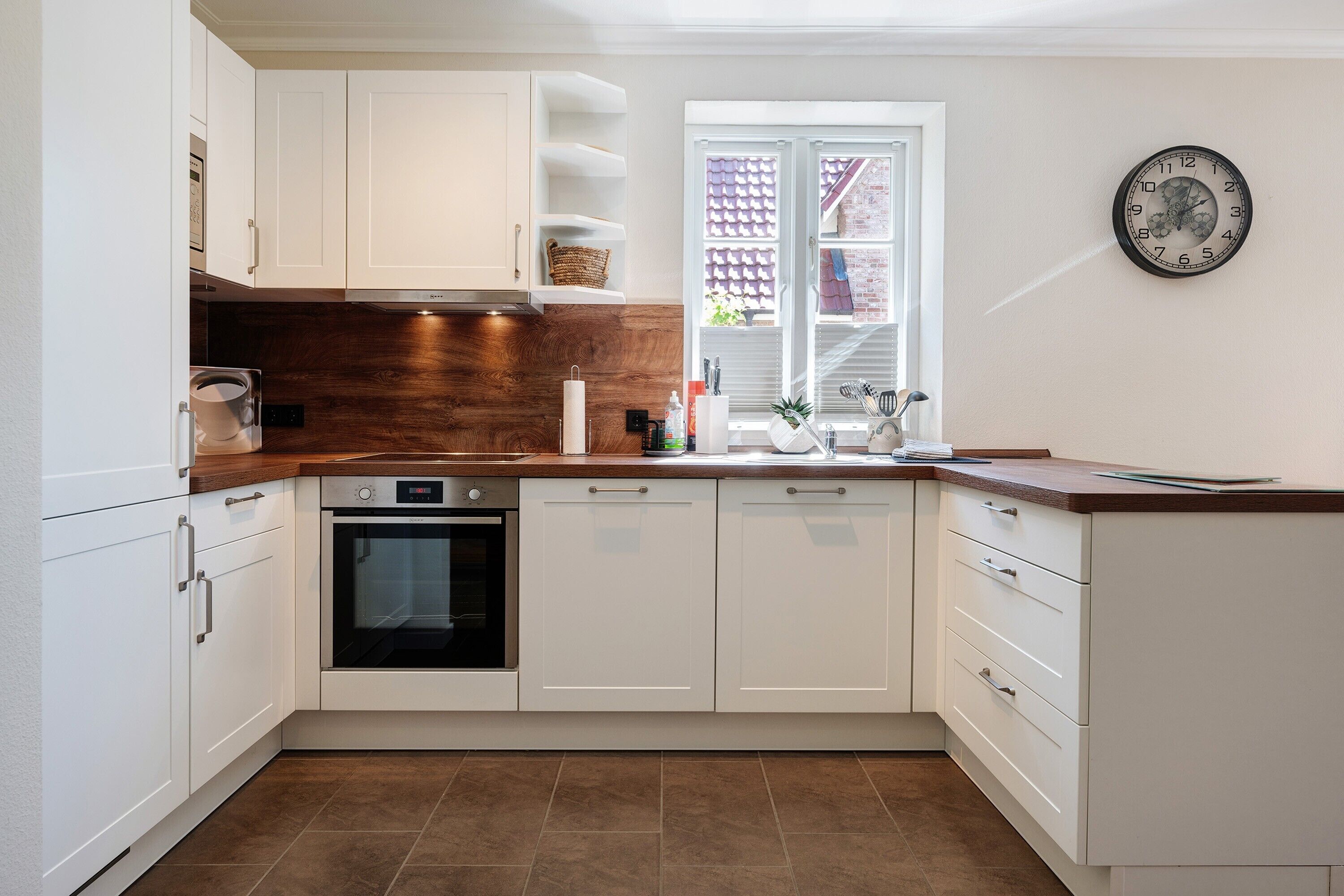 A modern kitchen with white cabinets, a wooden countertop, an oven, and a window with a view.