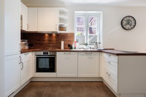 A modern kitchen with white cabinets, a wooden countertop, an oven, and a window with a view.