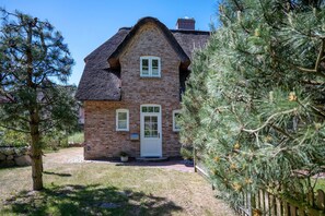 A brick house with a white door and windows, surrounded by a well-maintained lawn and trees.