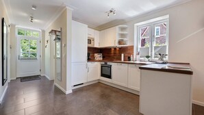 A modern kitchen with white cabinetry, a built-in oven, and a window with a view of a brick building. - Holiday Home 'Huus Alex' with Private Terrace, Private Garden and Wi-Fi (St. Peter-Ording Dorf)