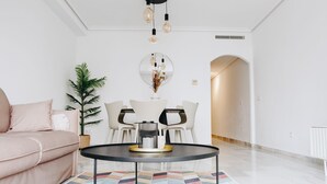 En moderne stue med en sofa, spisebord, stole, en potteplante, et spejl og en lampe i loftet.