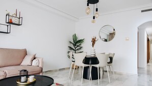 En moderne stue med sofa, sofabord, spisebord, stole, en potteplante og et spejl.