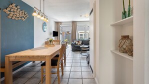 A modern kitchen with a wooden table and chairs, a blue accent wall, and a dining area with a sofa and a TV. - Düün Drööm – Your Dream House Behind the Dunes (St. Peter-Ording Dorf)