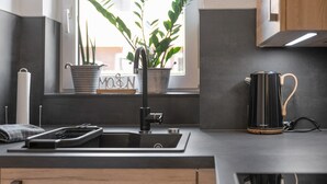 A modern kitchen with a black sink, a kettle, and a potted plant on the windowsill. - Düün Drööm – Your Dream House Behind the Dunes (St. Peter-Ording Dorf)